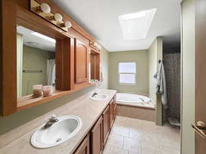 Bathroom with tile patterned flooring, vanity, a skylight, and a relaxing tiled tub