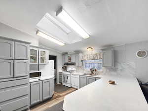 Kitchen featuring sink, lofted ceiling with skylight, white appliances, gray cabinets, and light wood-type flooring