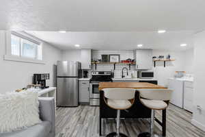 Kitchen featuring a kitchen bar, appliances with stainless steel finishes, sink, and washing machine and clothes dryer