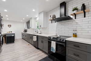 Kitchen featuring range with electric cooktop, sink, wall chimney range hood, stacked washer / dryer, and dishwasher