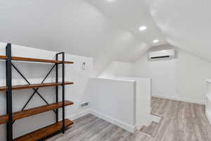 Additional living space with lofted ceiling, light laminate wood-type flooring, a textured ceiling, and a wall mounted mini split