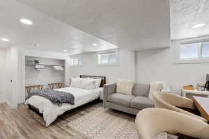 Bedroom with a textured ceiling, light wood-type flooring, a closet, and multiple windows