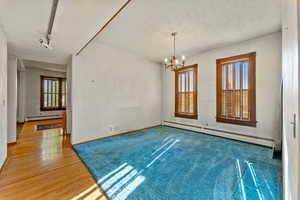 Empty room with hardwood / wood-style flooring, a notable chandelier, and a baseboard radiator