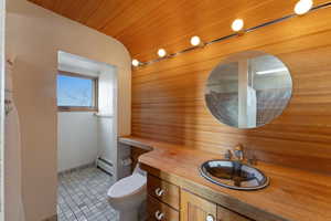 Bathroom with wood walls, tile patterned flooring, toilet, a baseboard radiator, and wood ceiling