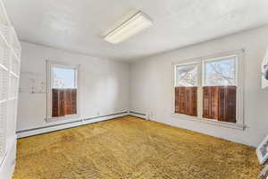 Carpeted empty room with a wealth of natural light and a baseboard heating unit