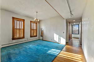 Spare room featuring baseboard heating, rail lighting, wood-type flooring, and an inviting chandelier