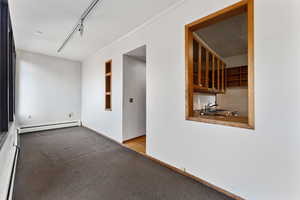 Carpeted empty room featuring baseboard heating, track lighting, and ornamental molding