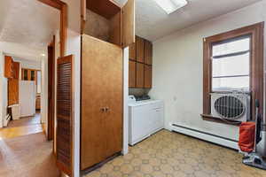 Laundry room with cabinets, washing machine and dryer, a textured ceiling, and a baseboard heating unit