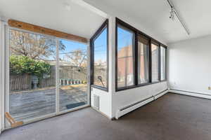 Unfurnished sunroom featuring a healthy amount of sunlight, lofted ceiling, and a baseboard heating unit