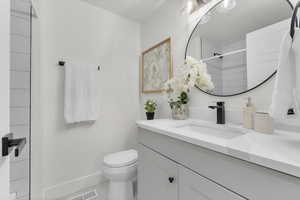 Bathroom with tiled shower, tile patterned flooring, vanity, and toilet