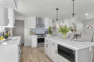 Kitchen with white cabinets, wall chimney exhaust hood, stainless steel appliances, and a kitchen island