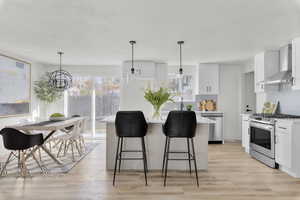 Kitchen featuring white cabinets, wall chimney exhaust hood, appliances with stainless steel finishes, and a chandelier