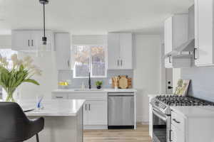 Kitchen featuring sink, wall chimney range hood, pendant lighting, white cabinets, and appliances with stainless steel finishes