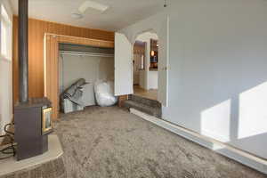 Bedroom with wood walls, a wood stove, carpet flooring, white fridge with ice dispenser, and a closet