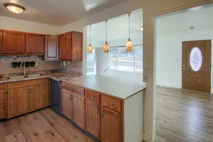 Kitchen featuring dishwasher, sink, hanging light fixtures, tasteful backsplash, and light wood-type flooring