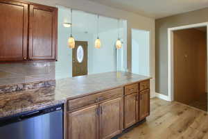 Kitchen featuring dishwasher, decorative backsplash, light wood-type flooring, and decorative light fixtures