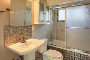 Full bathroom featuring sink, tasteful backsplash, toilet, and bath / shower combo with glass door