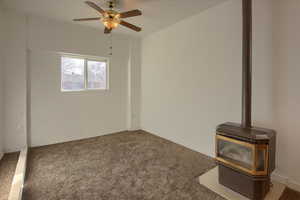 Carpeted empty room featuring ceiling fan and a wood stove