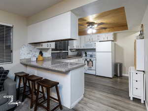 Kitchen featuring kitchen peninsula, white cabinetry, sink, and white appliances