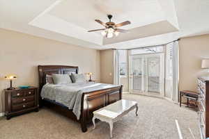 Carpeted bedroom with a raised ceiling and ceiling fan