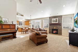 Carpeted living room featuring ceiling fan with notable chandelier, a healthy amount of sunlight, a fireplace, and vaulted ceiling