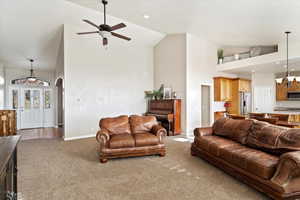 Living room featuring ceiling fan with notable chandelier, carpet floors, and high vaulted ceiling