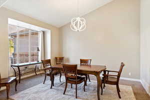 Dining area featuring light colored carpet, vaulted ceiling, and an inviting chandelier