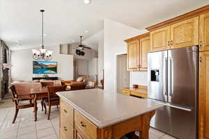 Kitchen with stainless steel fridge, ceiling fan with notable chandelier, vaulted ceiling, light tile patterned floors, and a kitchen island