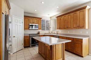 Kitchen with a textured ceiling, a kitchen island, stainless steel appliances, and light tile patterned floors