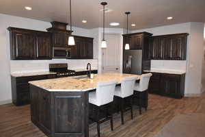 Kitchen featuring dark brown cabinetry, a center island with sink, stainless steel appliances, and decorative light fixtures