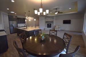 Dining room with a stone fireplace, sink, ceiling fan with notable chandelier, and dark hardwood / wood-style flooring