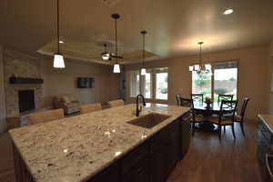 Kitchen featuring a raised ceiling, sink, a kitchen island with sink, and dark wood-type flooring