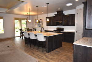 Kitchen featuring a center island with sink, hanging light fixtures, dark hardwood / wood-style floors, dark brown cabinets, and gas stove