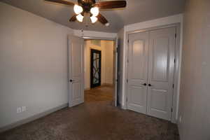 Unfurnished bedroom featuring a closet, dark carpet, and ceiling fan