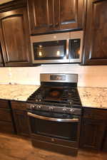 Kitchen featuring dark brown cabinetry, dark wood-type flooring, and appliances with stainless steel finishes