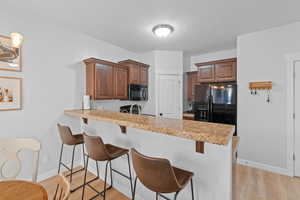 Kitchen with kitchen peninsula, a textured ceiling, a breakfast bar, black appliances, and light wood-type flooring