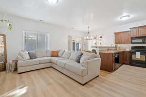 Living room with a textured ceiling, an inviting chandelier, light hardwood / wood-style flooring, and sink