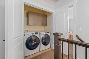 Clothes washing area featuring cabinets, light tile patterned flooring, and washing machine and clothes dryer