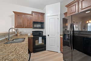 Kitchen featuring light stone countertops, a textured ceiling, sink, black appliances, and light hardwood / wood-style floors