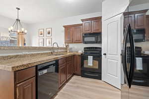 Kitchen with kitchen peninsula, sink, black appliances, an inviting chandelier, and light hardwood / wood-style floors