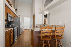 Kitchen with dark wood-type flooring, a kitchen breakfast bar, light stone counters, kitchen peninsula, and stainless steel appliances