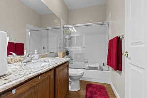 Full bathroom featuring hardwood / wood-style floors, vanity, toilet, and bath / shower combo with glass door