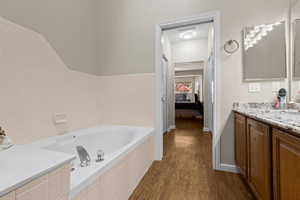 Bathroom with hardwood / wood-style floors, vanity, and a relaxing tiled tub