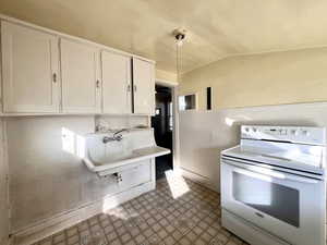 Kitchen featuring white range with electric cooktop, white cabinetry, hanging light fixtures, and lofted ceiling