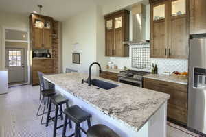 Kitchen with sink, wall chimney exhaust hood, light stone countertops, appliances with stainless steel finishes, and decorative light fixtures