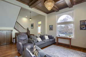 Living room featuring dark hardwood / wood-style floors, beam ceiling, ornamental molding, and an inviting chandelier