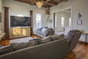 Living room with a chandelier, beam ceiling, hardwood / wood-style flooring, and decorative columns