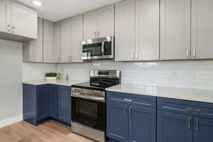 Kitchen with blue cabinetry, decorative backsplash, light hardwood / wood-style flooring, and appliances with stainless steel finishes