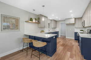 Kitchen featuring pendant lighting, light wood-type flooring, blue cabinetry, appliances with stainless steel finishes, and kitchen peninsula