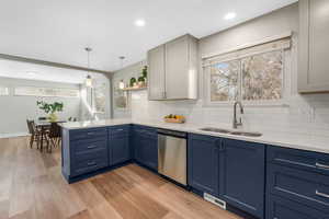 Kitchen with blue cabinetry, sink, stainless steel dishwasher, kitchen peninsula, and pendant lighting